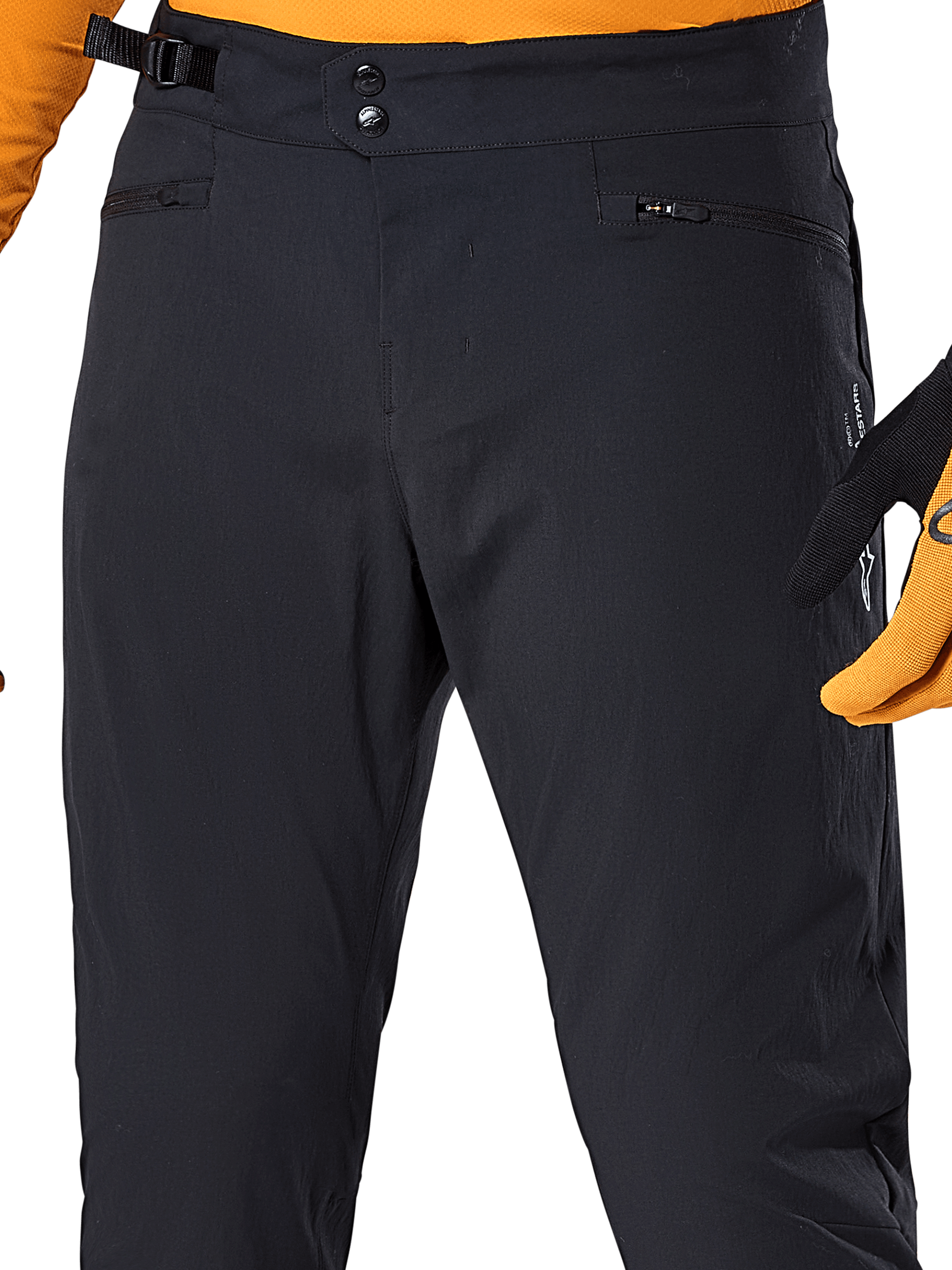 Alpinestars A-Dura Pants, Black MTB cycling pants, close-up view featuring double snap waist closure, adjustable side cinch, and zippered pockets, paired with an orange jersey and gloves