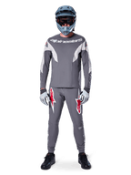 MTB rider wearing Alpinestars A-Supra Race Pants in Dark Gray, featuring bold red logo accents on the thighs, paired with a matching gray jersey, blue full-face helmet, and black shoes for a complete off-road racing kit