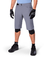 Alpinestars A-Dura Shorts, Dark Gray Mountain Bike Shorts, paired with black gloves and knee guards, featuring zippered pockets and double snap closure, rugged cycling gear for off-road trails