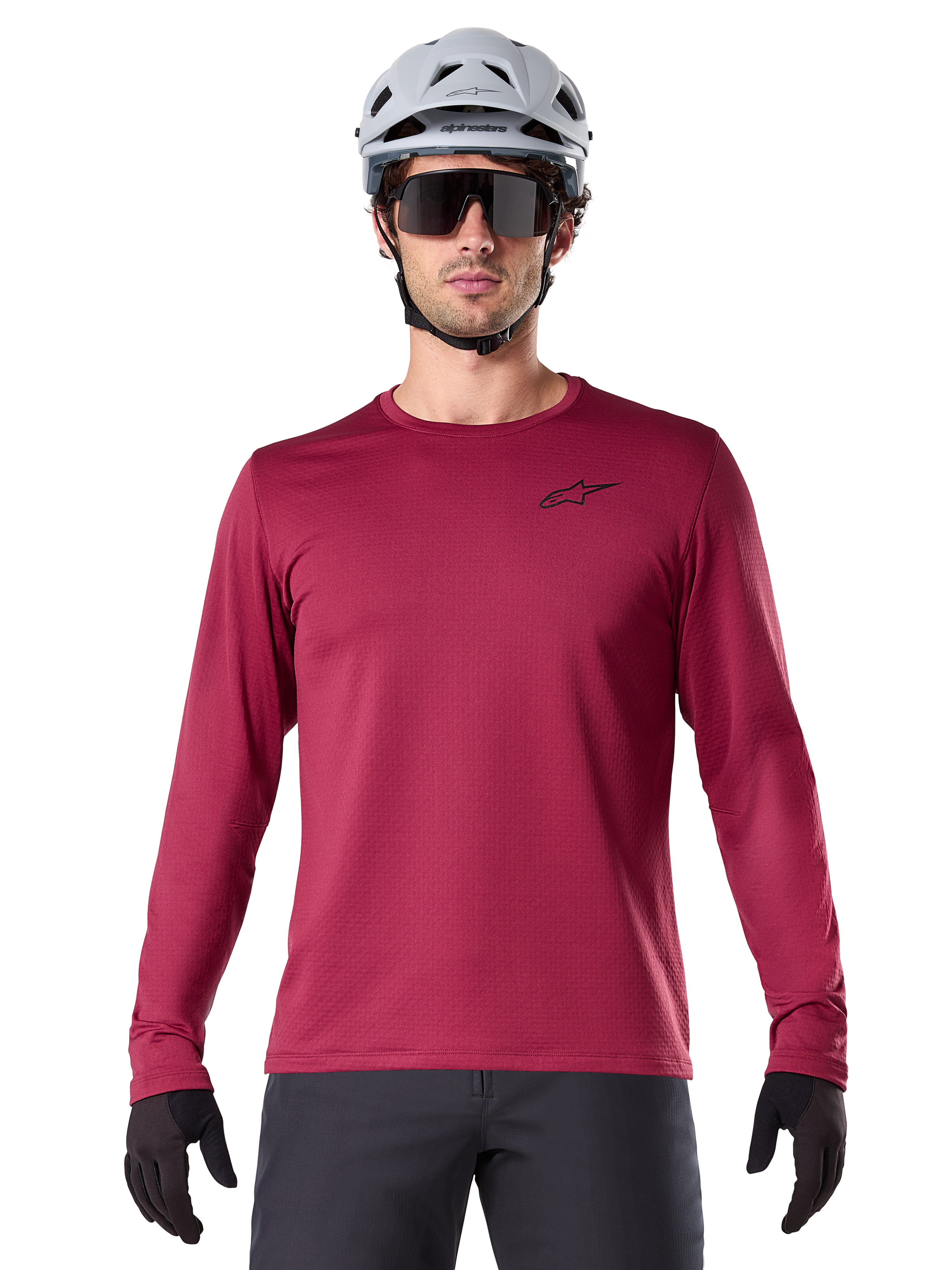 Male cyclist wearing Alpinestars A-Dura Thermal Jersey, Long Sleeve MTB Jersey, Burgundy, styled with a gray helmet and black sunglasses, features a small black star logo on the chest, insulated fleece fabric for cold-weather mountain biking