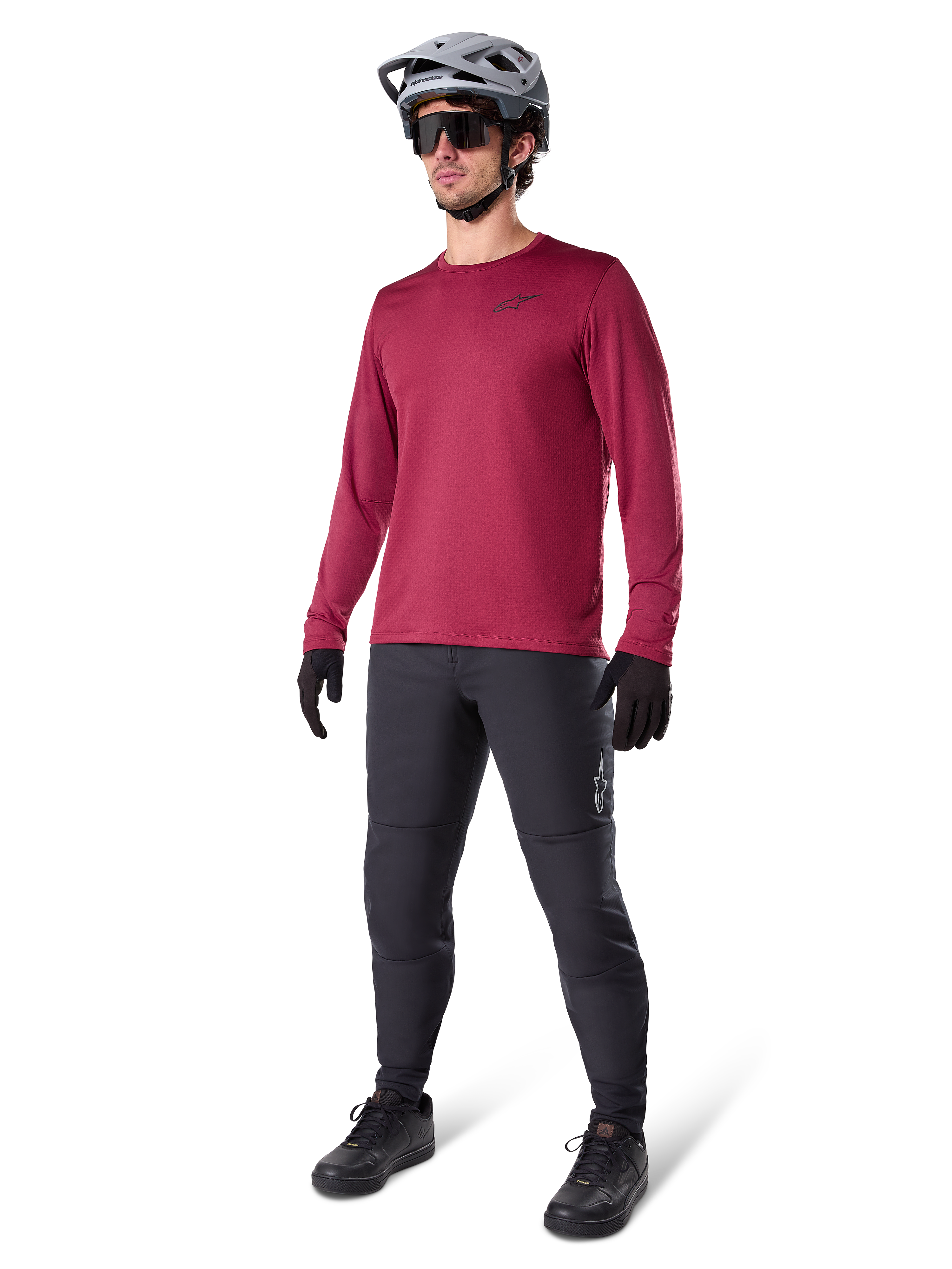 Alpinestars A-Dura Thermal Jersey in Burgundy, long-sleeve insulated cycling top worn with dark grey mountain bike pants, black gloves, and a grey helmet, full-body studio shot of cold-weather MTB gear.