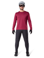 Male model wearing Alpinestars A-Dura Thermal Jersey in Burgundy, long-sleeve insulated cycling top, paired with dark grey mountain bike pants, white helmet, black sunglasses, and black gloves, professional MTB gear for cold weather