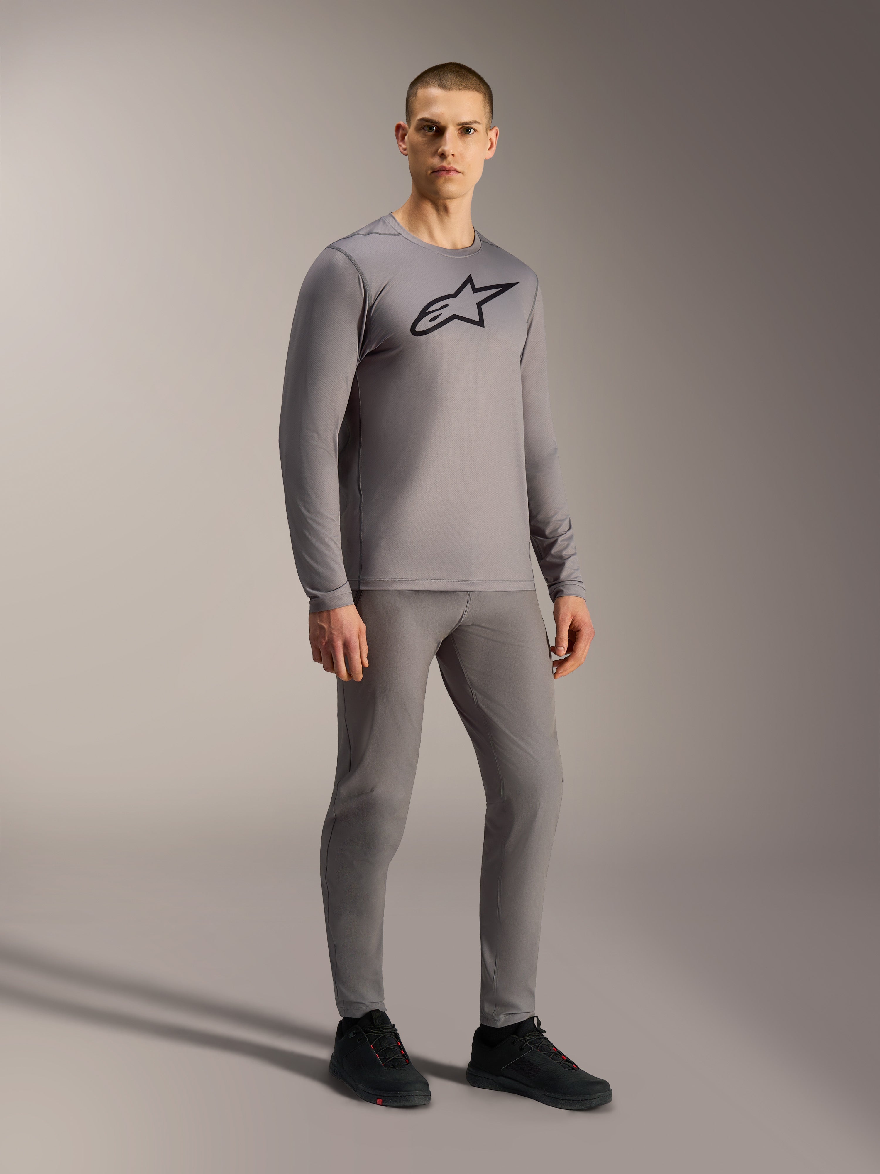 Gray A-Dura Ride Long Sleeve Jersey featuring a black chest logo, styled on a model for a complete mountain biking look.