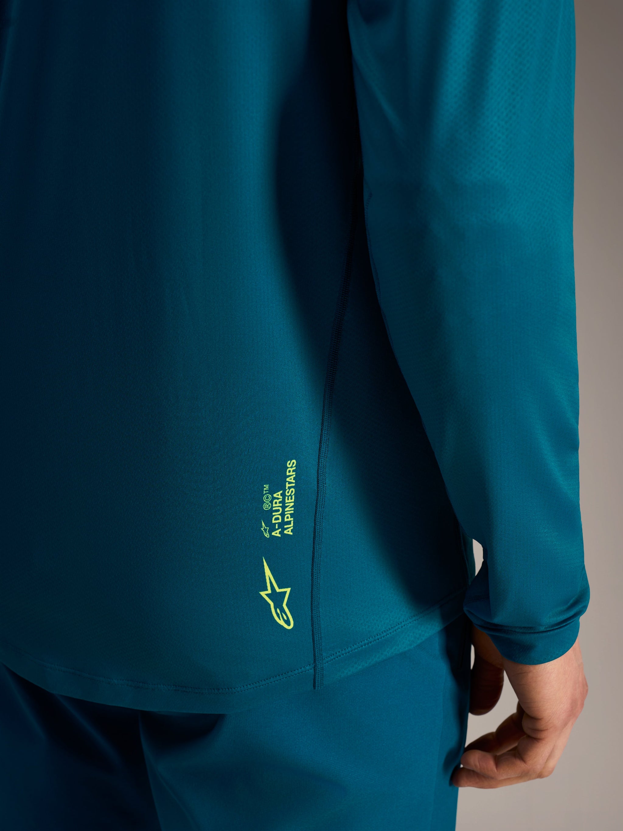 Blue Green A-Dura Ride Long Sleeve Jersey featuring lime green Alpinestars branding on the textured lower back hem.