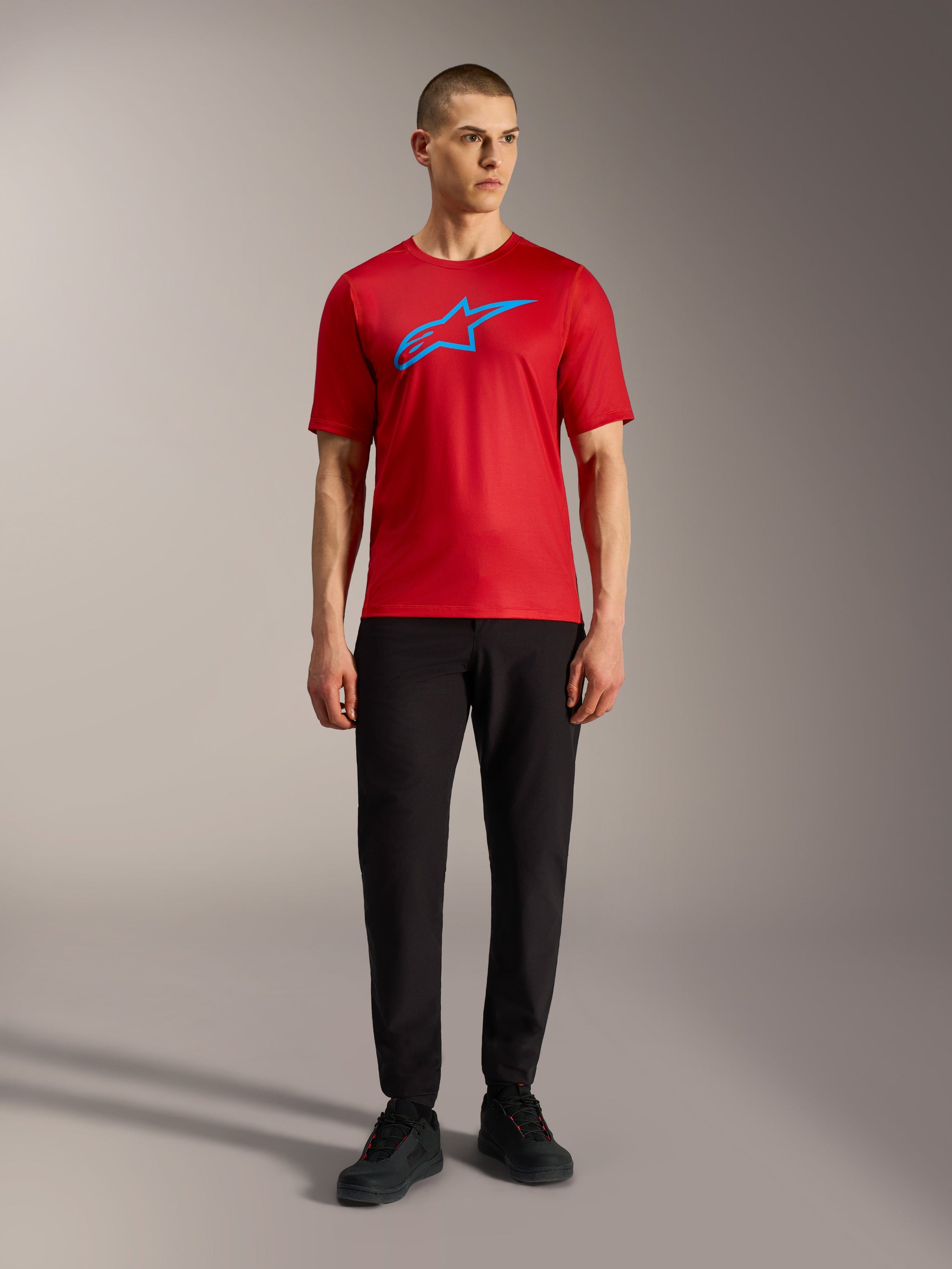 Red Alpinestars A-Dura Ride Short Sleeve Jersey with blue logo, styled with black pants for a casual MTB look.
