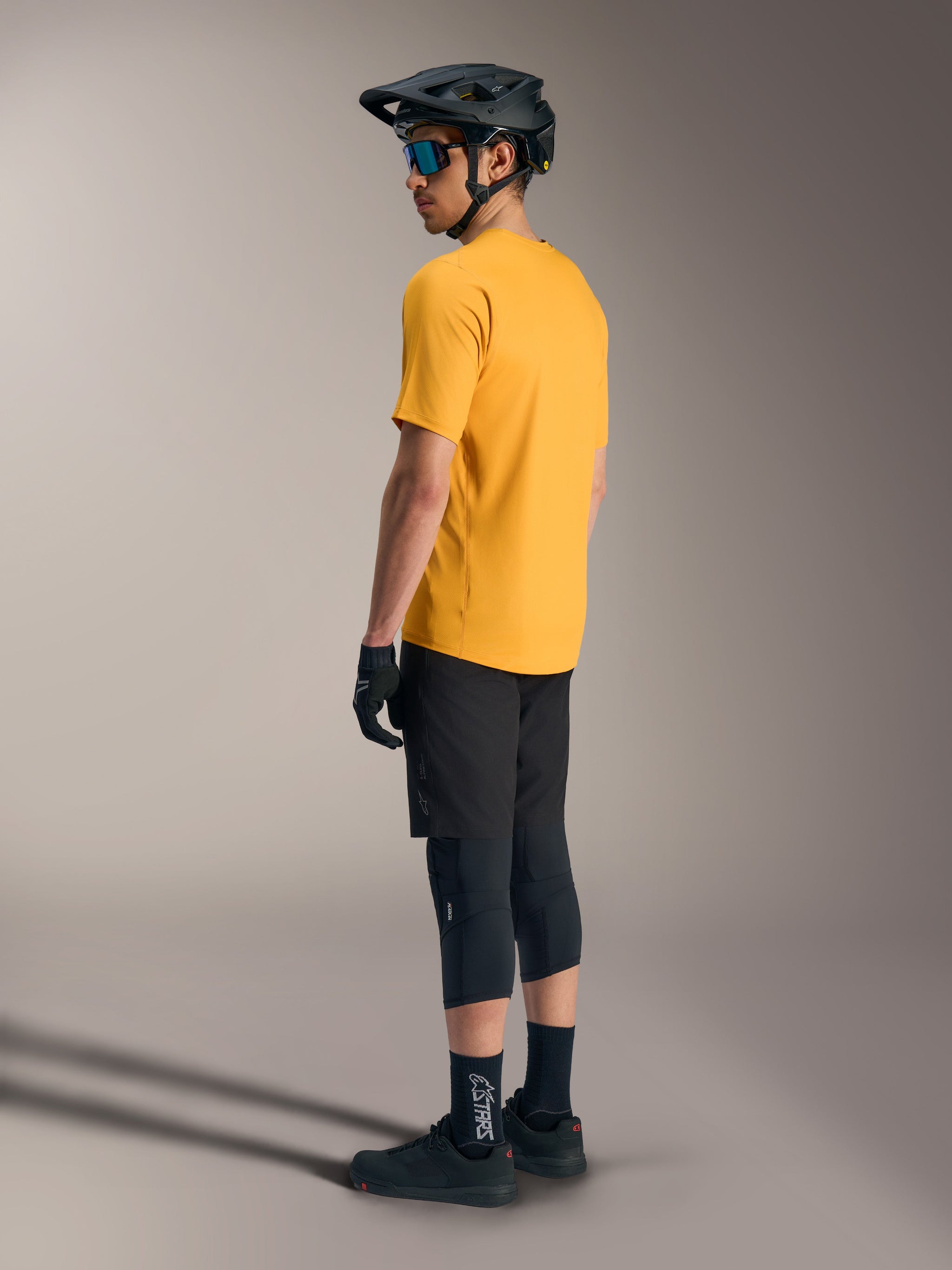 Alpinestars A-Dura Ride Short Sleeve Jersey in orange, shown from the back on a rider with black MTB gear and helmet.