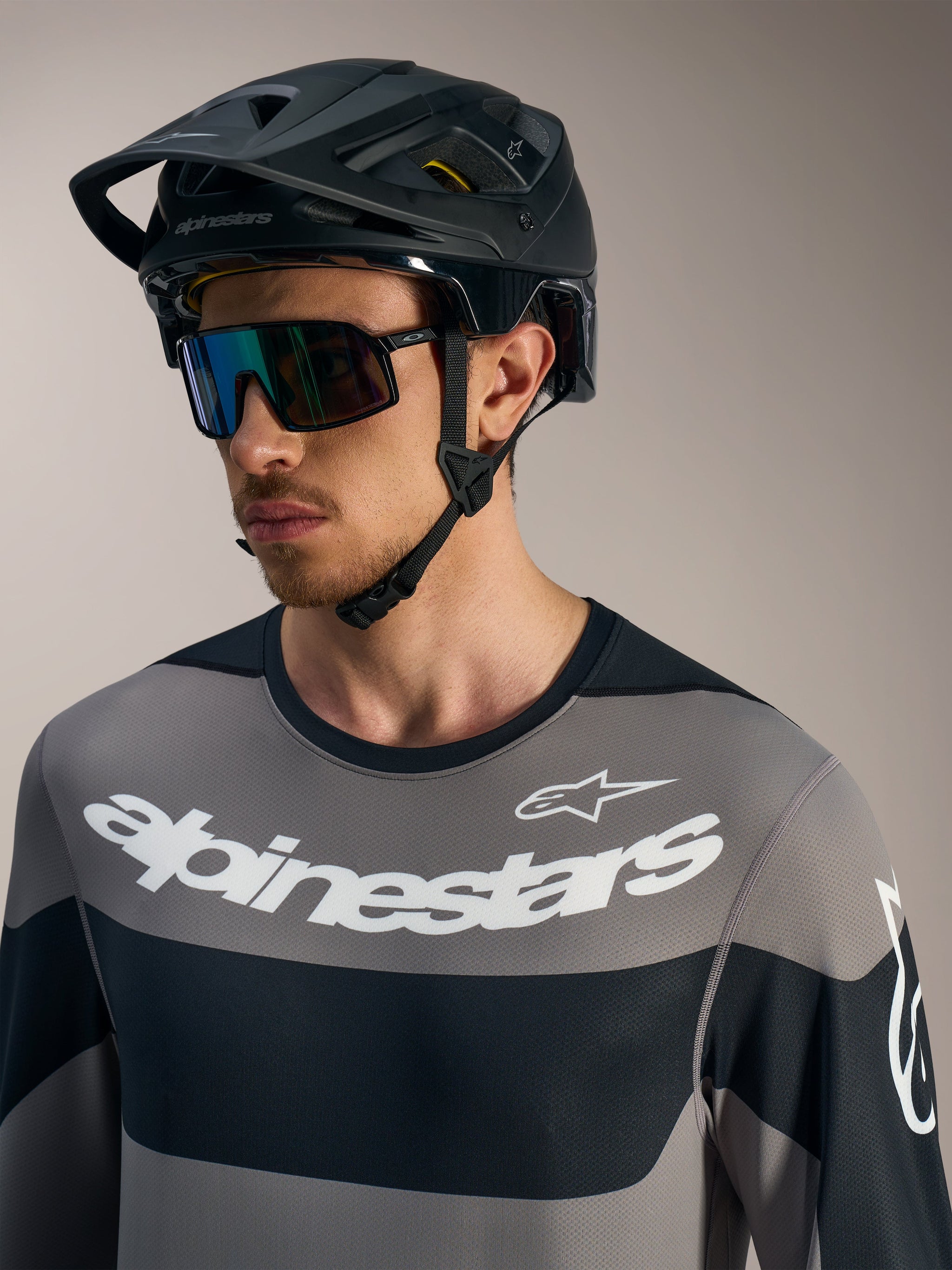 Alpinestars A-Dura Race Long Sleeve Jersey in gray with bold white logos, black MTB helmet, and performance sunglasses.