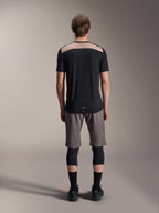 Alpinestars A-Dura Lipan Jersey - Short Sleeve, Black with tan upper back panel, rear view showing dropped tail, worn with grey MTB shorts and black knee guards, performance mountain bike apparel