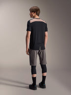 Alpinestars A-Dura Lipan Short Sleeve Jersey in Black, back view on model showcasing the light brown perforated mesh panel across the upper back, paired with grey mountain bike shorts and black knee guards for a complete trail riding outfit.