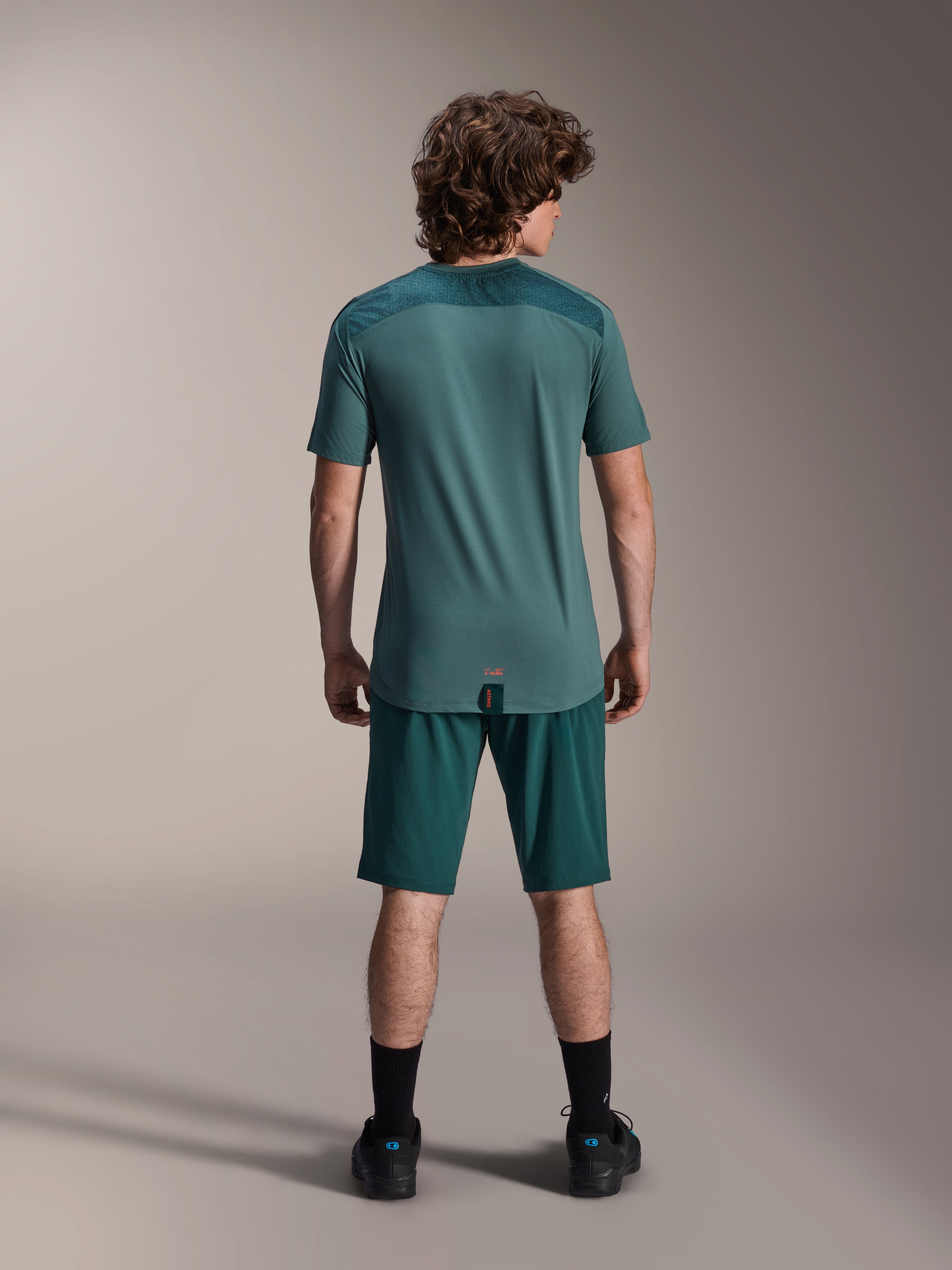 Alpinestars A-Dura Shorts and A-Dura Lipan SS Jersey, Dark Pine green, back view on a model, performance mountain bike apparel featuring short sleeve jersey and matching shorts, off-road cycling outfit