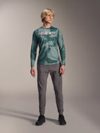 Alpinestars A-Dura Hollow Camo Long Sleeve Jersey, Silver Pine Camo with green camouflage pattern, large white "astars" logo on the chest, worn with gray technical pants and black riding shoes, high-performance MTB gear