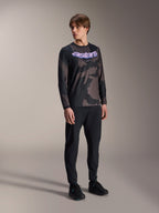 Male model wearing Alpinestars A-Dura Hollow Camo Long Sleeve Jersey, Black Camo pattern with purple 'astars' chest graphic, paired with black technical pants and black shoes, casual MTB gear