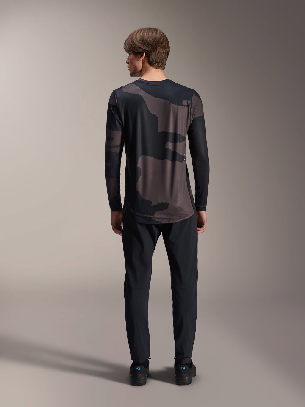 Alpinestars A-Dura Hollow Camo Long Sleeve Jersey, Black Camo, back view worn with black pants, featuring a dark camouflage pattern and dropped rear hem for MTB coverage.