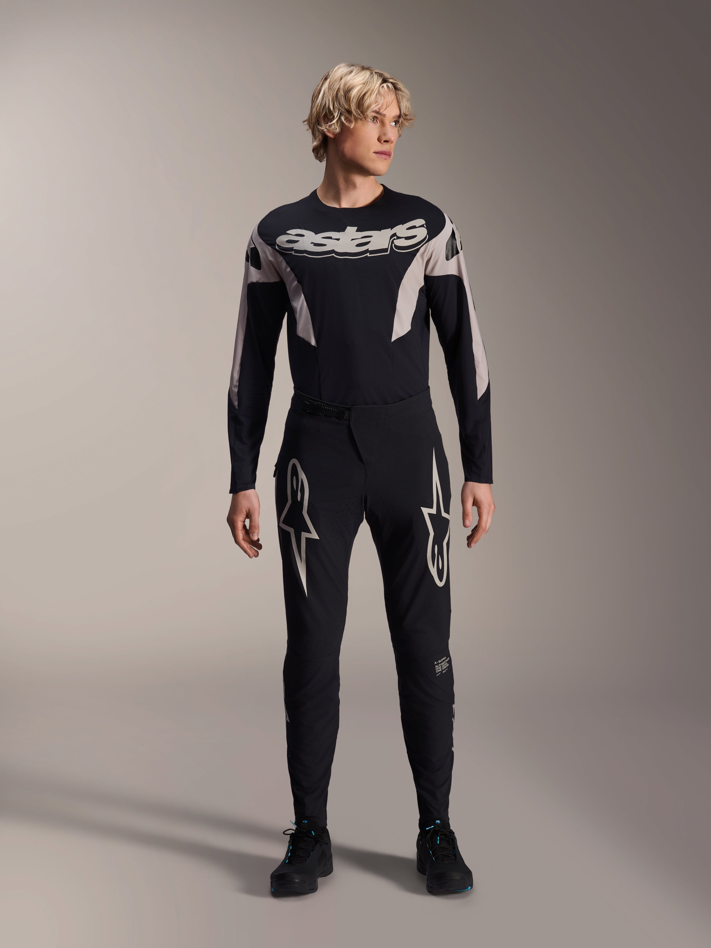 Alpinestars A-Supra Melt Pants and matching Long Sleeve Jersey, model wearing black MTB kit with large white star graphics on thighs and 'astars' branding on chest, professional mountain bike racing apparel.