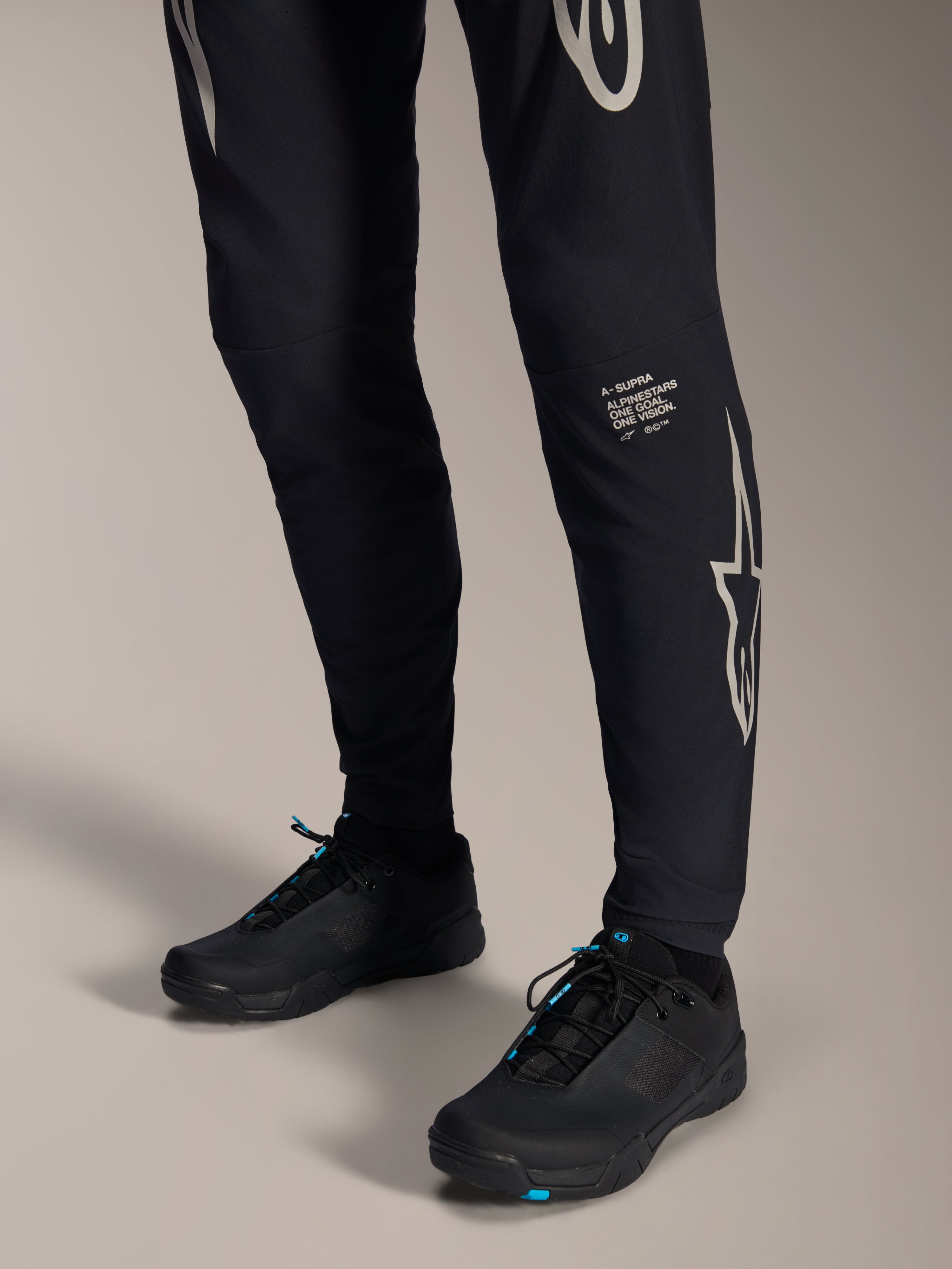 Alpinestars A-Supra Melt Pants, Black Mountain Bike Pants, featuring white Alpinestars wordmark and logo on the leg, worn with black cycling shoes with blue accents, performance off-road gear