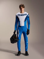 Male model wearing Alpinestars A-Supra Melt MTB kit, white and blue long-sleeve jersey with "astars" wordmark, blue A-Supra Melt pants with white logo, black full-face helmet, black gloves and shoes, coordinated off-road cycling outfit