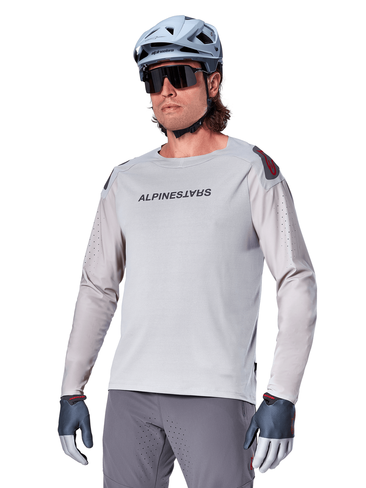 Alpinestars A-Aria Polartec Switch Jersey Long Sleeve, Light Gray cycling jersey with black chest logo and red shoulder accent, laser-perforated sleeves for airflow, worn with a light blue helmet, sunglasses, and gray pants, performance mountain bike apparel for trail riding