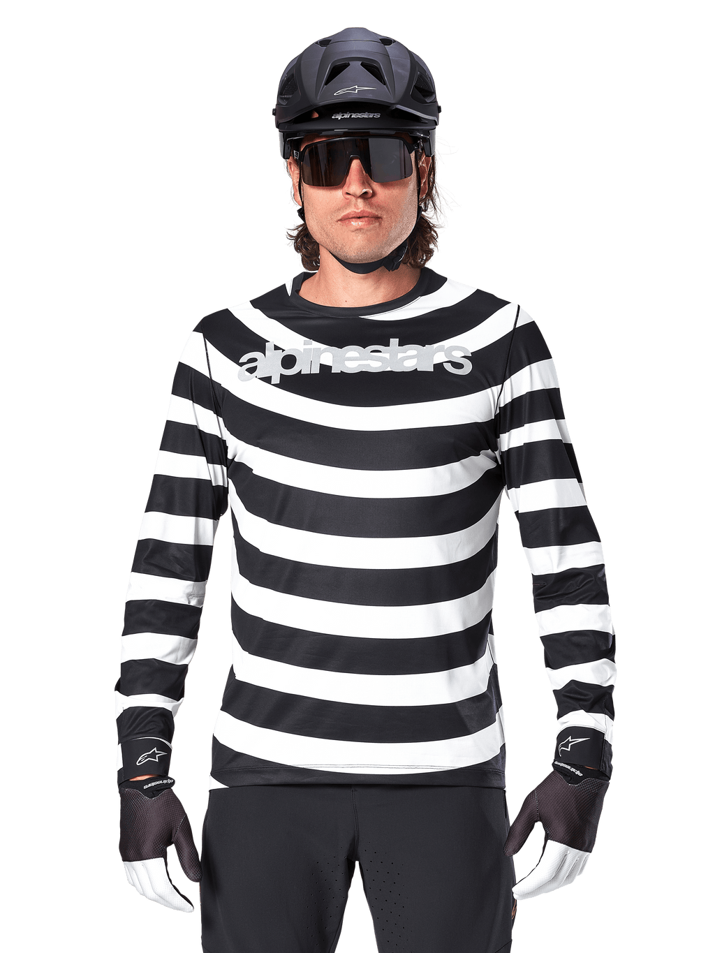 Male cyclist wearing Alpinestars A-Aria Oscar Long Sleeve Jersey, Black and White horizontal stripes, reflective Alpinestars logo on the chest, styled with a black MTB helmet, cycling sunglasses, and performance gloves