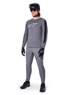 Alpinestars A-Dura Dri Astar Jersey, Long Sleeve MTB Jersey, Dark Gray with white chest logo, black mesh panels on sleeves, worn with matching gray pants, black helmet, and gloves, performance mountain bike apparel