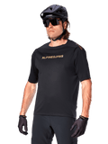 Alpinestars A-Aria Polartec Switch Jersey Short Sleeve, Black mountain bike jersey with gold Alpinestars branding, worn with black helmet, sunglasses, and gloves, technical MTB apparel