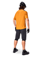 Alpinestars A-Aria Polartec Switch Jersey, Short Sleeve MTB Jersey, Dark Gold, rear view of model wearing dark gray mountain bike shorts, black helmet, and gloves, technical cycling apparel for off-road trails