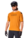 Alpinestars A-Aria Polartec Switch Jersey, Short Sleeve MTB Jersey, Dark Gold with black branding, worn by model with black helmet, sunglasses, and cycling gloves, high-performance mountain bike apparel