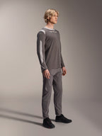 Male model wearing Alpinestars A-Dura Dri Wool Long Sleeve Jersey in Dark Gray, paired with matching gray pants and black shoes, featuring light gray mesh panels on the shoulders and sleeves, technical MTB gear for off-road cycling