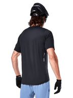 Alpinestars A-Dura Oscar Jersey, Short Sleeve cycling jersey, Black, rear view on rider, paired with light blue shorts and black MTB helmet, small white logo on the side, performance apparel for mountain biking