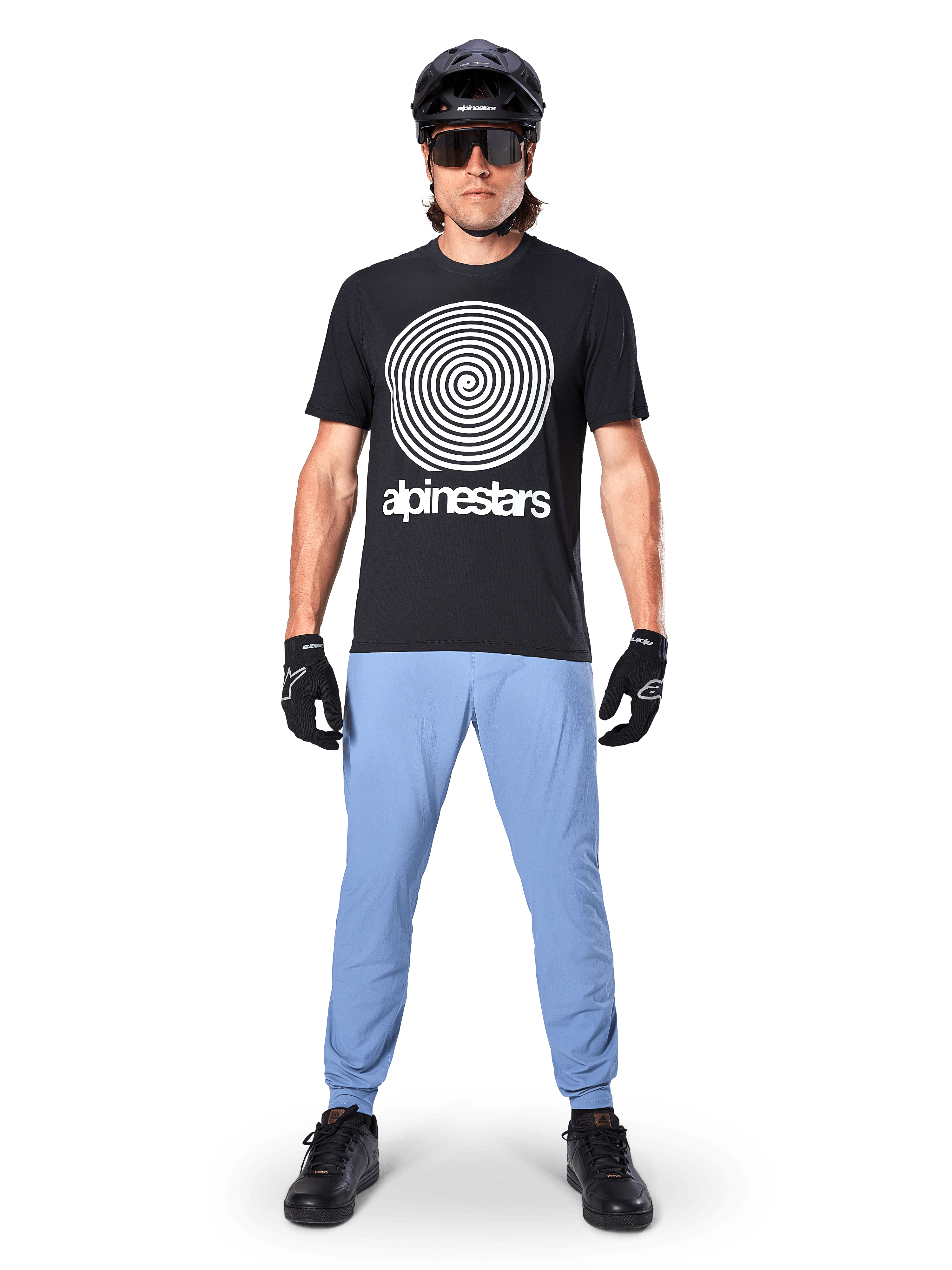 Alpinestars A-Dura Oscar Jersey - Short Sleeve, Black MTB Jersey, featuring a large white vintage Oscar spiral graphic and brand text, worn with light blue pants, black helmet, sunglasses, and black gloves, performance mountain bike apparel