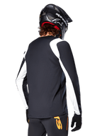 MTB rider wearing Alpinestars A-Supra Oscar Long Sleeve Jersey, Black with white panels on the shoulders and sleeves, viewed from behind, black helmet and gloves, pants with orange accents, durable off-road cycling apparel