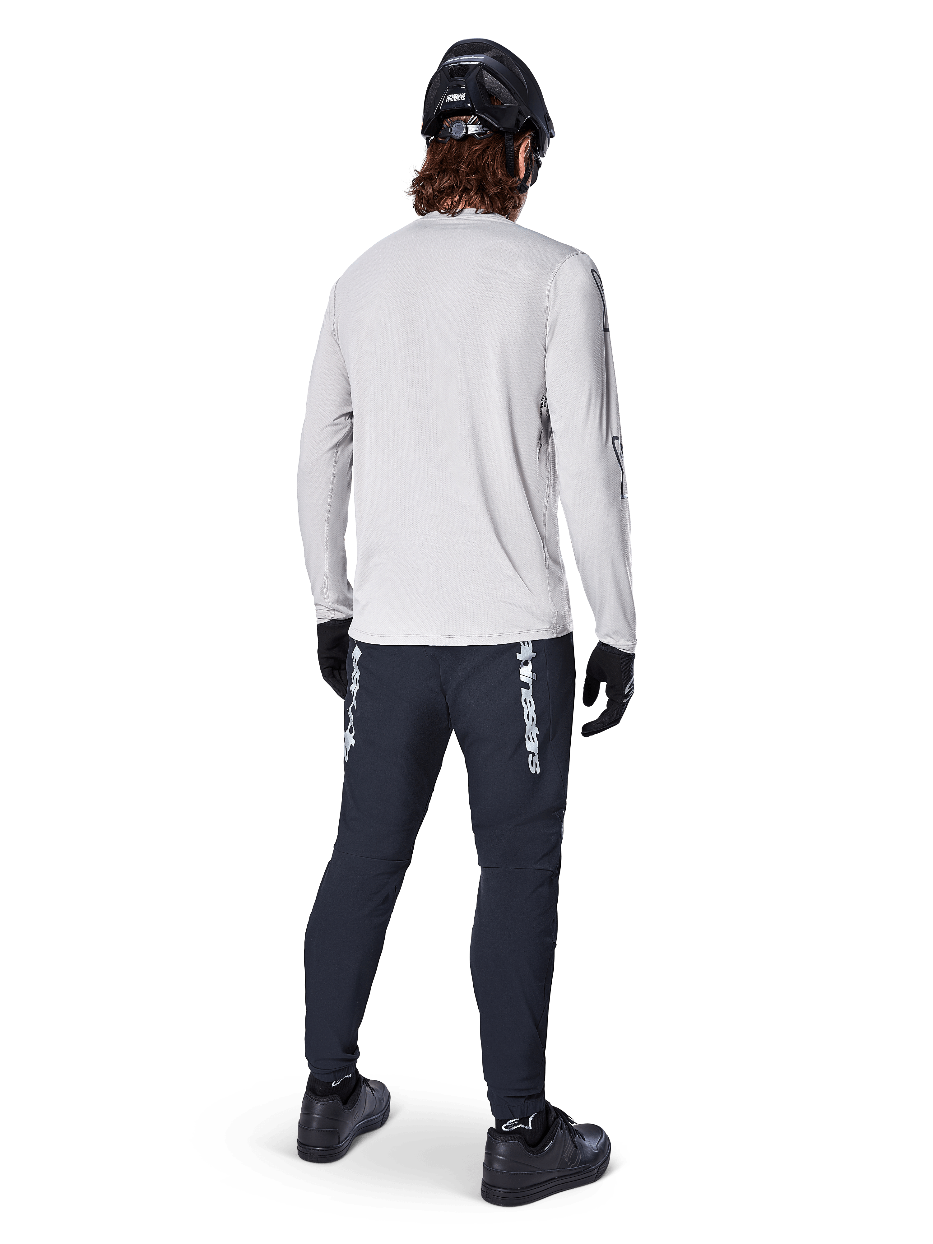 Alpinestars A-Dura Switch Long Sleeve Jersey, Light Gray, rear view on a rider wearing black cycling pants, helmet, and gloves, high-performance mountain bike gear with a longer drop tail.