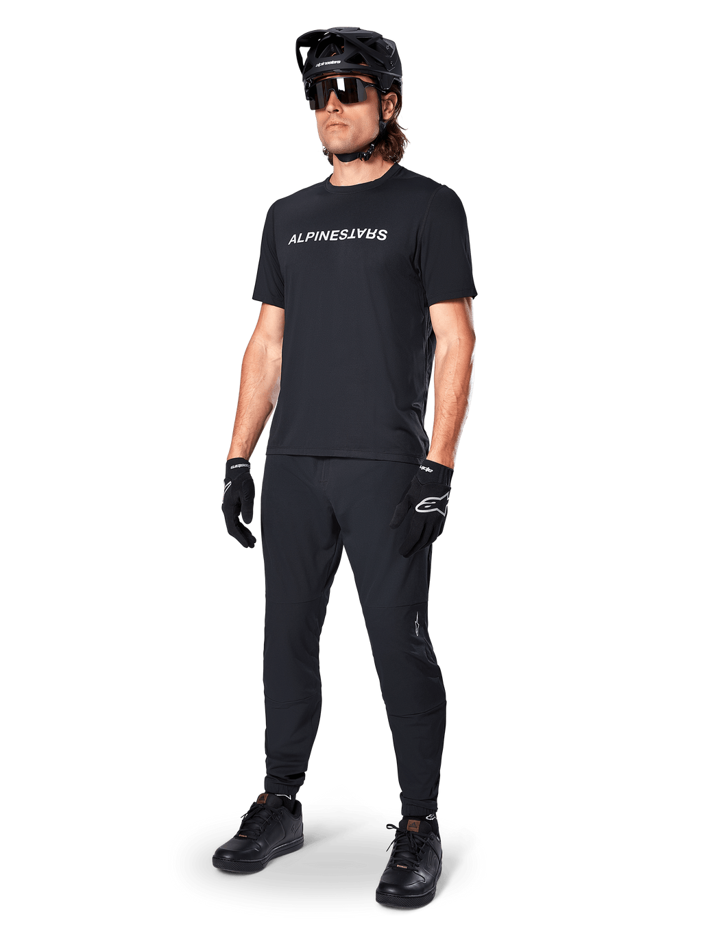 Alpinestars A-Dura Switch Short Sleeve Jersey, Black, worn by model with matching black MTB pants, helmet, and gloves, featuring a white Alpinestars wordmark on the chest, performance mountain bike apparel