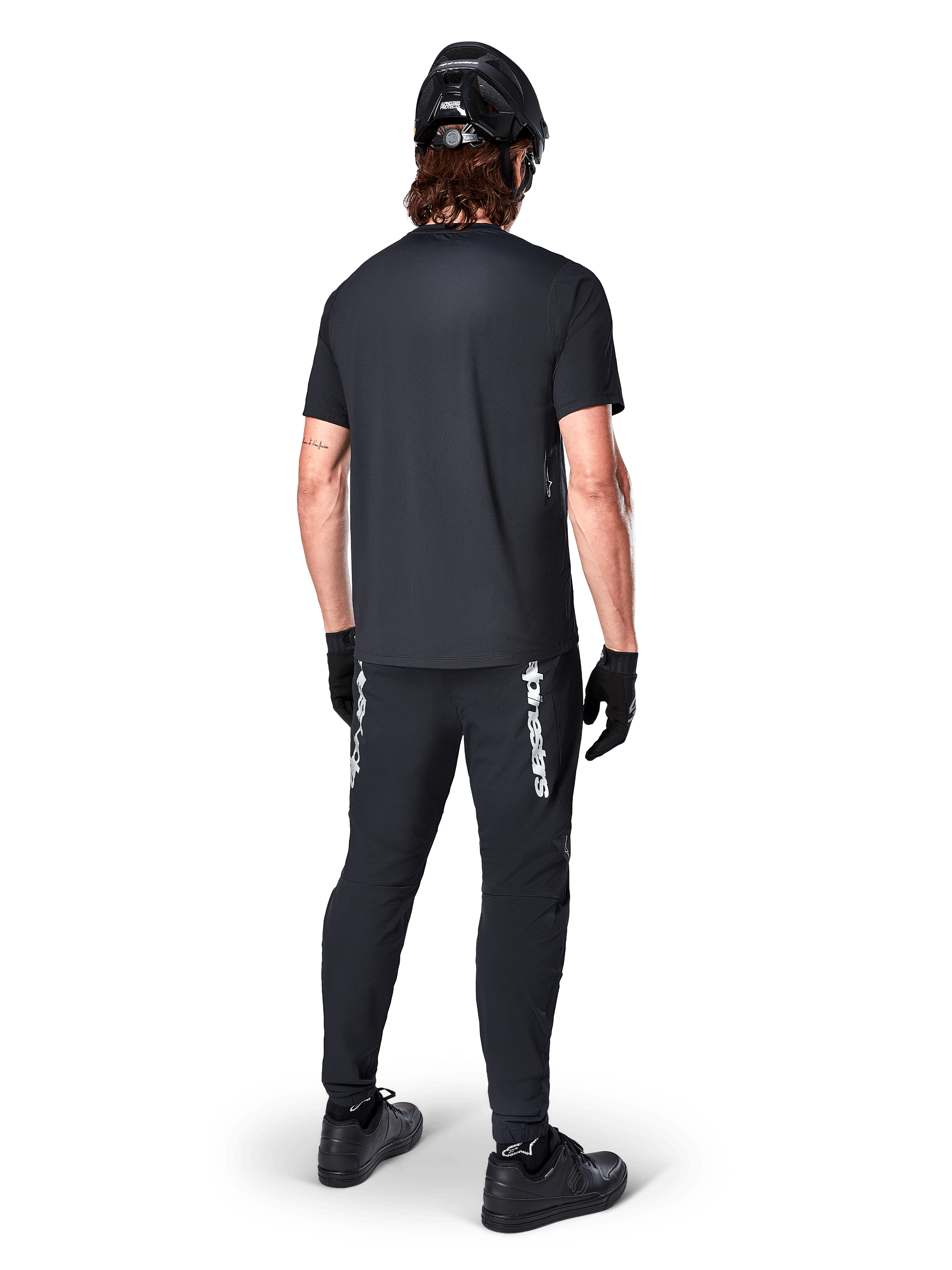 Alpinestars A-Dura Switch Jersey - Short Sleeve, Black, back view of rider wearing complete mountain bike gear, including matching black pants with white wordmark branding, black helmet, and gloves, performance cycling apparel for trail riding