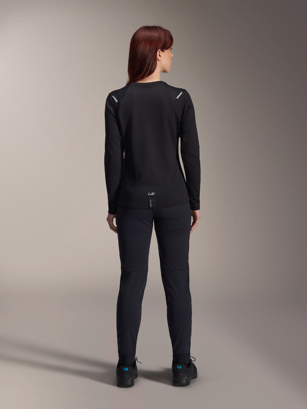 Alpinestars Woman Stella A-Dura Thermal Jersey, Back View, Black, Long-sleeve cycling jersey with insulated fleece, worn with matching black pants and shoes, featuring small A-Dura branding on the lower back and reflective shoulder accents, tailored for women's MTB riding.
