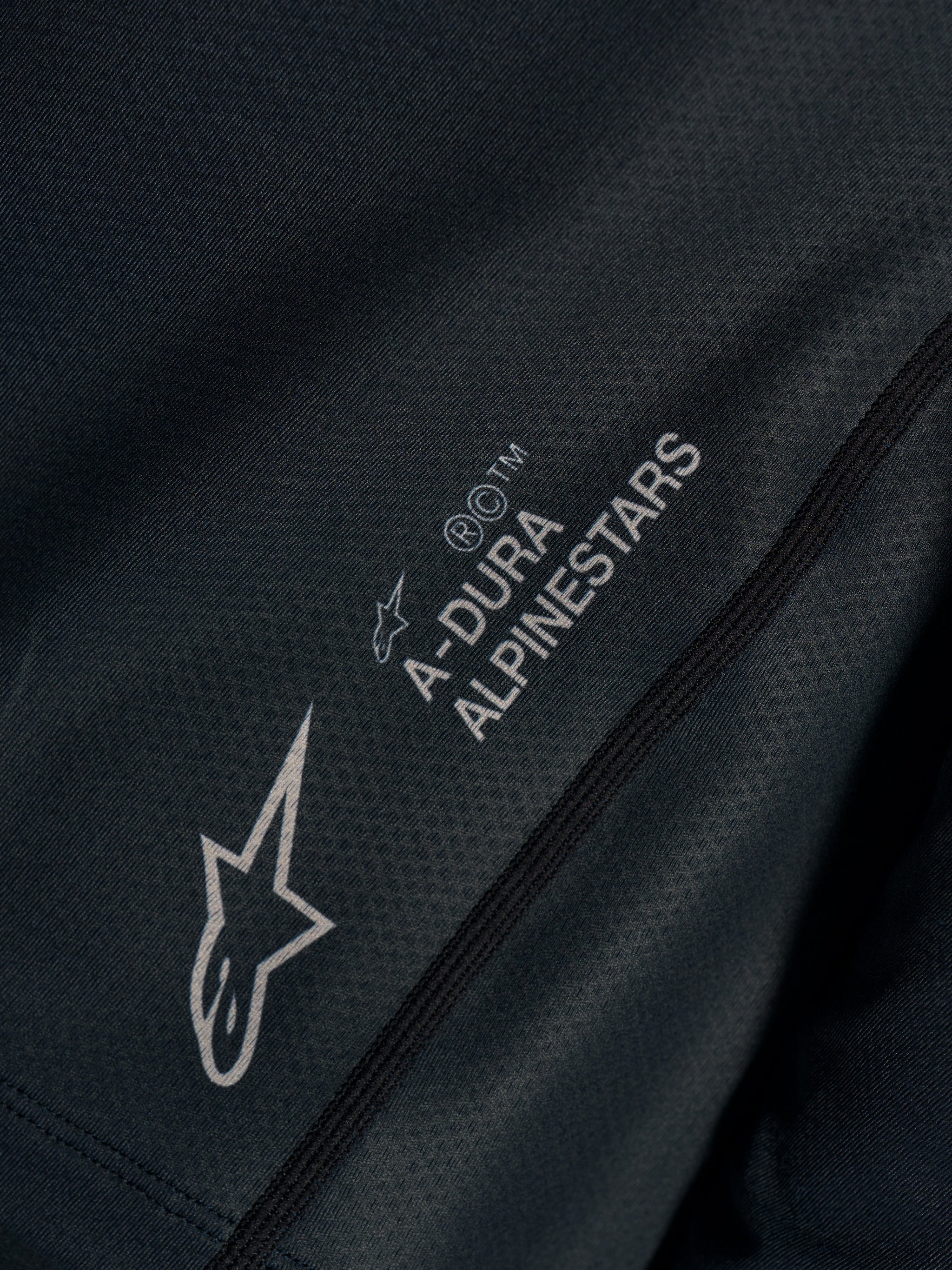 Black Stella A-Dura Ride Jersey close-up, showing technical jacquard fabric with A-DURA ALPINESTARS and Astars logos.