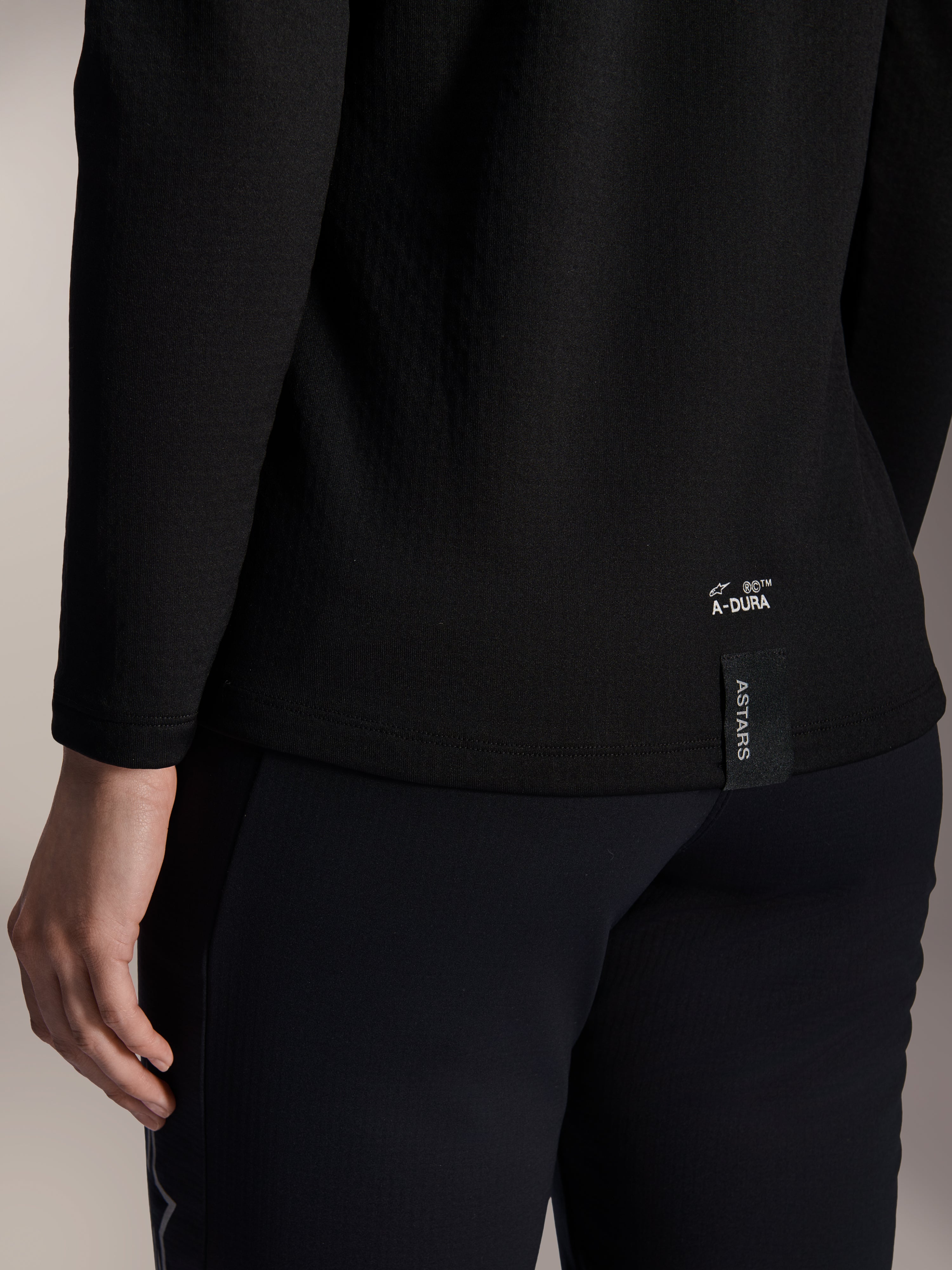 Alpinestars Woman Stella A-Dura Thermal Jersey, Black Thermal MTB Jersey, close-up of back lower hem with white A-DURA branding and vertical ASTARS logo tag, designed for cold weather mountain biking