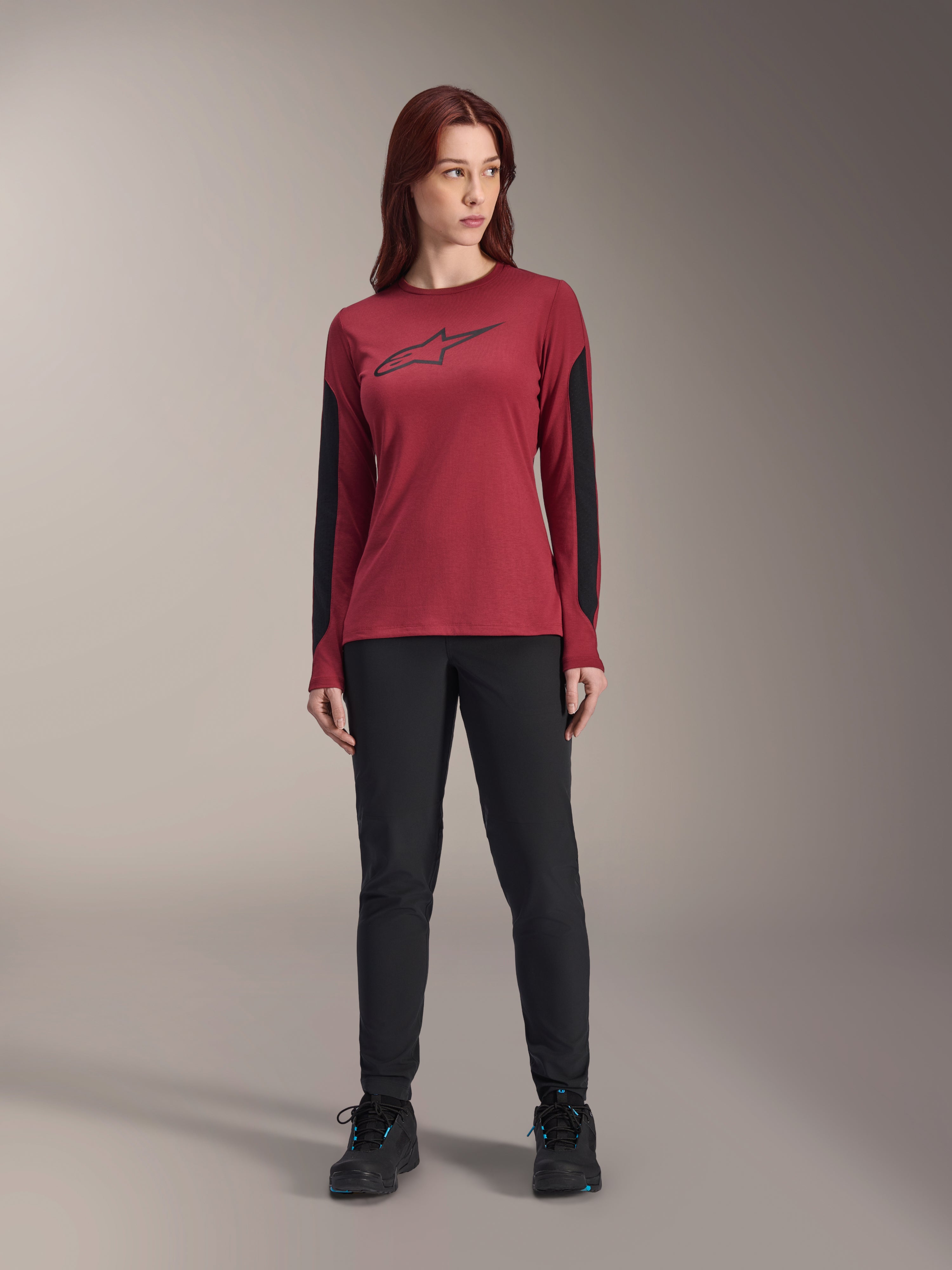 Alpinestars Women Stella A-Dura Dri Astar Long Sleeve Jersey in Burgundy, featuring a black Astars logo on the chest and black mesh arm panels, styled with black technical pants and athletic shoes, performance mountain bike apparel for women.