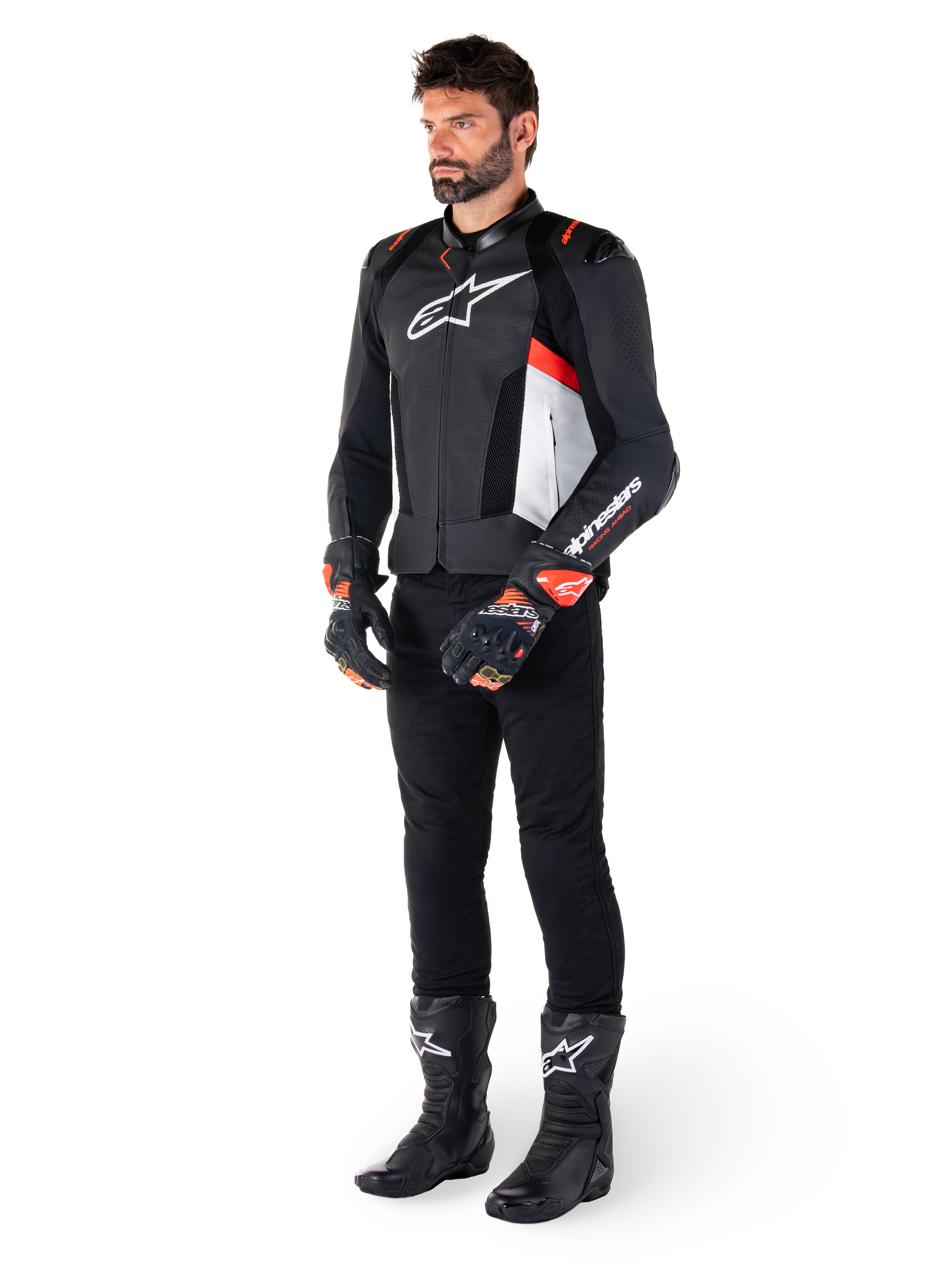 Alpinestars Missile V3 Airflow Leather Jacket, Black White Red Fluo, worn by a male model with black pants, black racing gloves, and black boots, featuring perforated leather for ventilation, a white chest logo, and red fluo accents, designed for premium racing and sport performance.