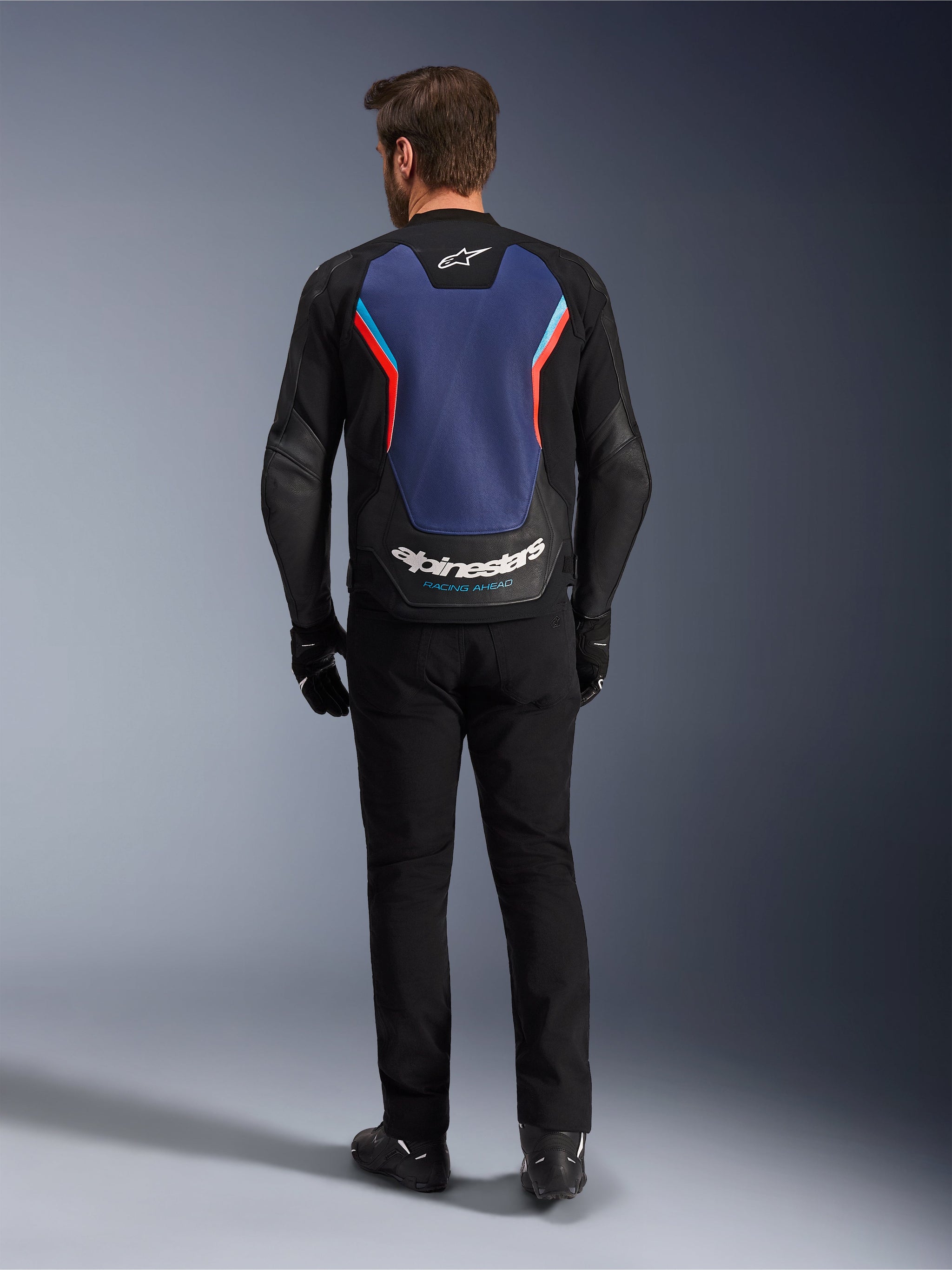 Alpinestars GP Force V2 Leather Jacket, Sport Motorcycle Jacket, Black Blue Red Fluo, back view on a model, featuring a large blue back panel with red and light blue accents and white Alpinestars branding at the lower back, paired with black riding pants and gloves.