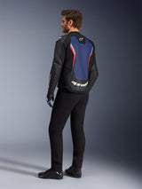 Rear three-quarter view of a male model wearing the Alpinestars GP Force V2 Leather Jacket in Black Blue Red Fluo, highlighting the blue back panel with red fluorescent accents and white branding, styled with black pants and motorcycle gloves.