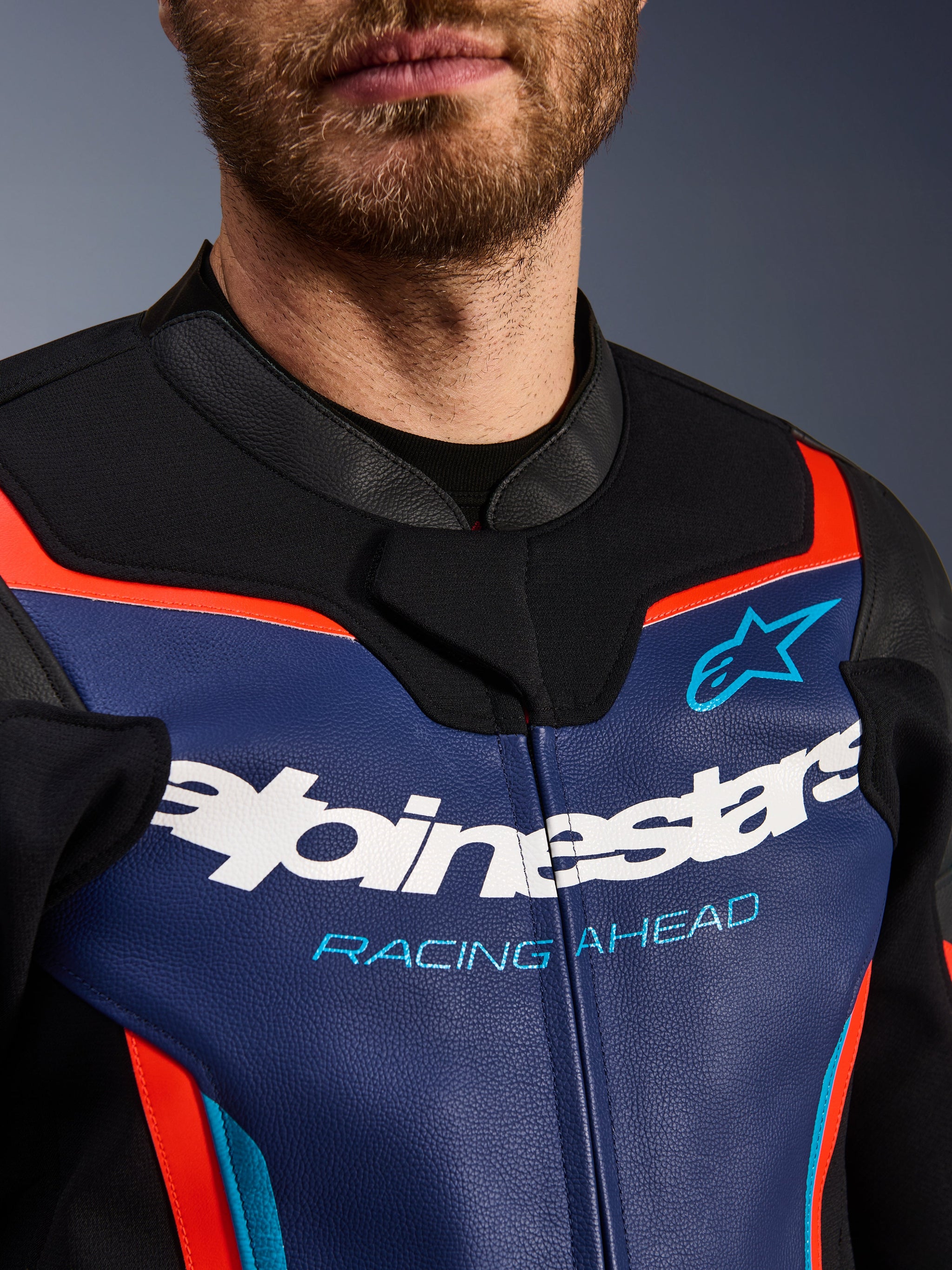 Alpinestars GP Force V2 Leather Jacket, detail view of chest and collar, Blue Black and Red Fluo, featuring white Alpinestars logo and light blue 'RACING AHEAD' text, premium leather texture with fluorescent accents