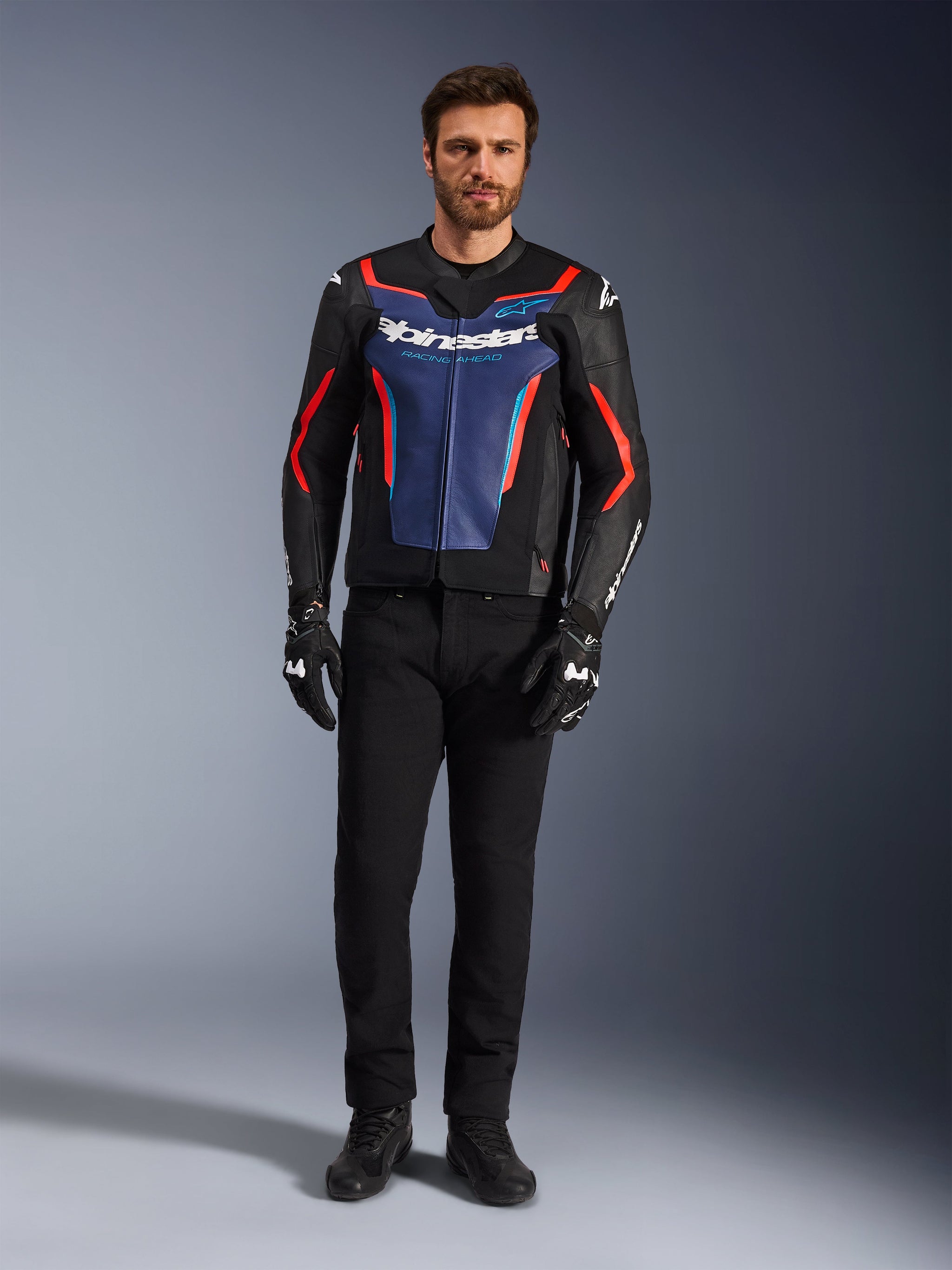 Alpinestars GP Force V2 Leather Jacket, Black Blue and Red Fluo, worn by a male model with black pants and riding gloves, sport motorcycle jacket featuring bovine leather and racing-inspired design, front view