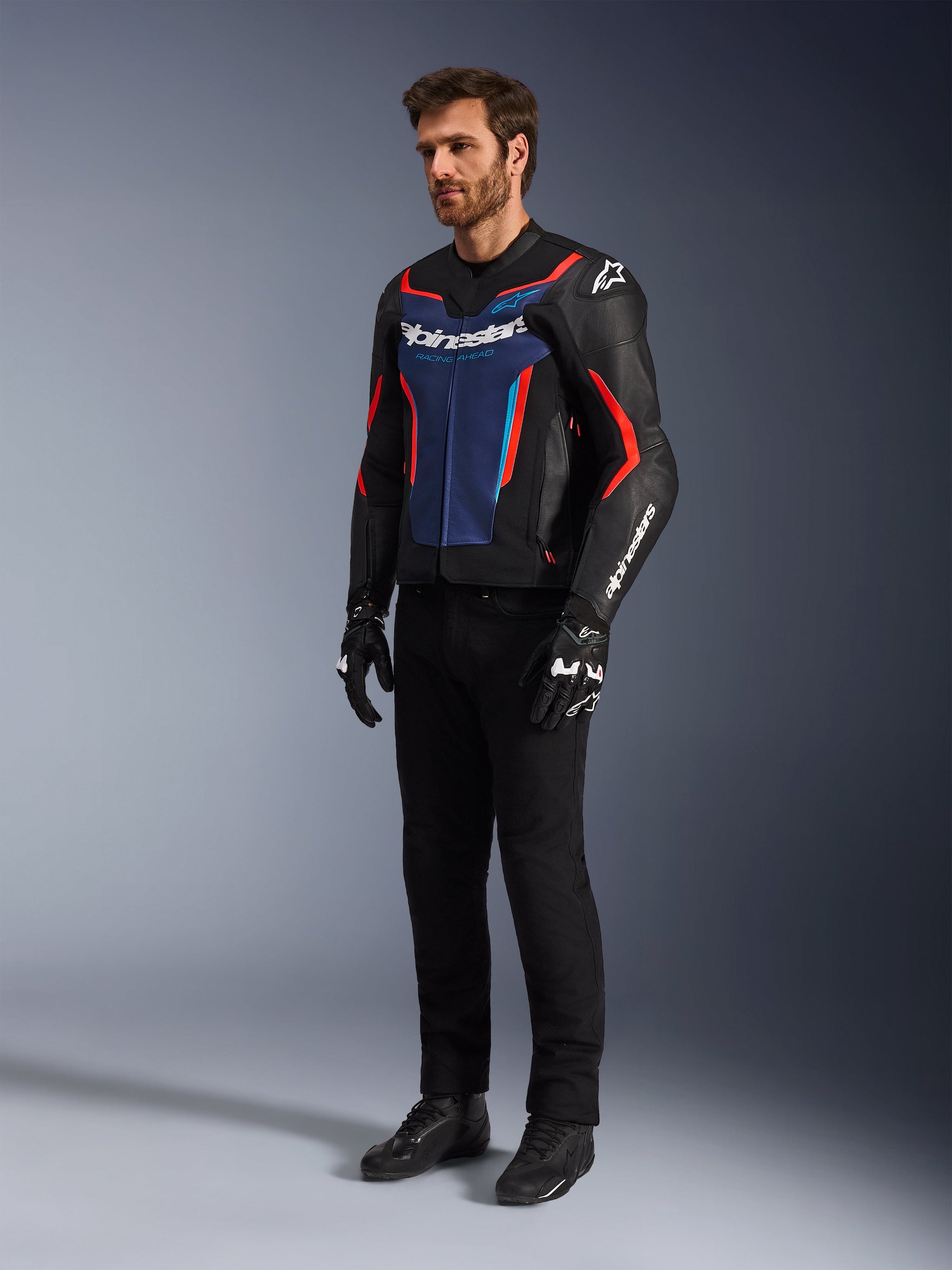 Model wearing the Alpinestars GP Force V2 Leather Jacket in Black Blue Red Fluo, paired with black technical riding pants, black gloves, and boots, professional motorcycle racing gear for sport riding
