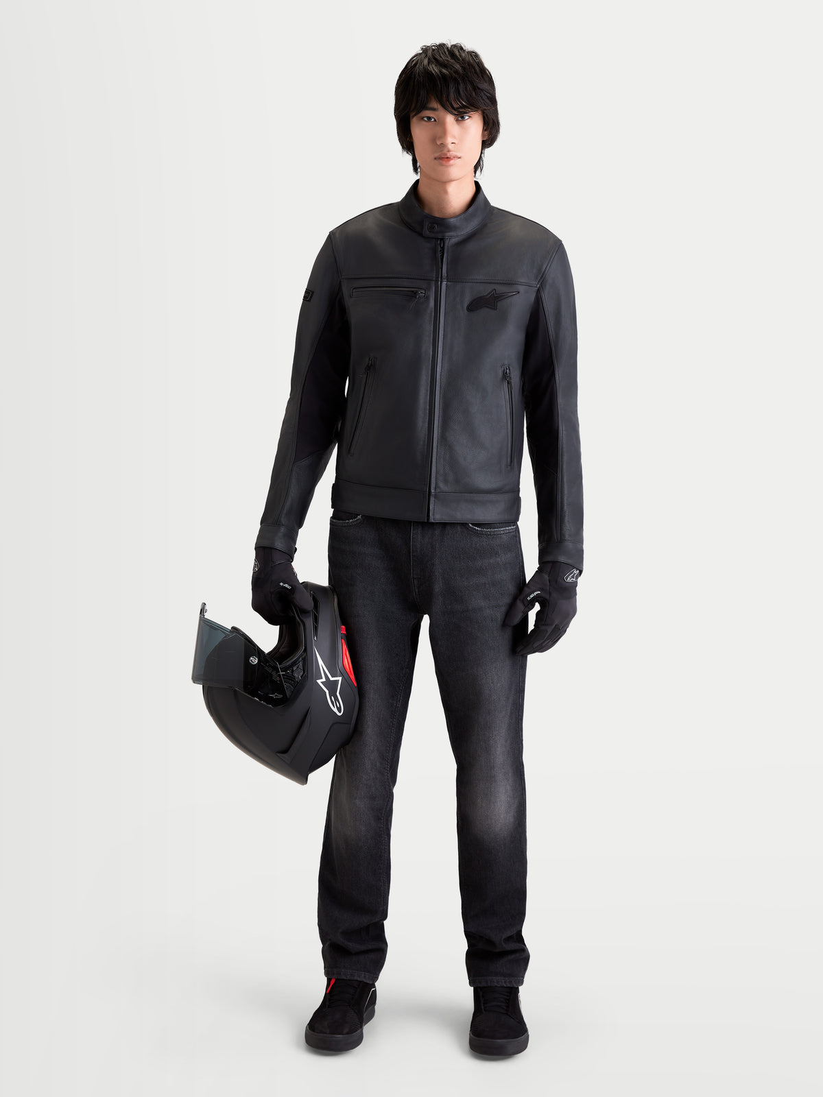 Alpinestars Maver-X Leather Jacket, men's urban contemporary motorcycle leather jacket in black, front view on a model wearing matching gloves, dark jeans, and holding a helmet, featuring a premium soft bovine leather construction and biker collar.