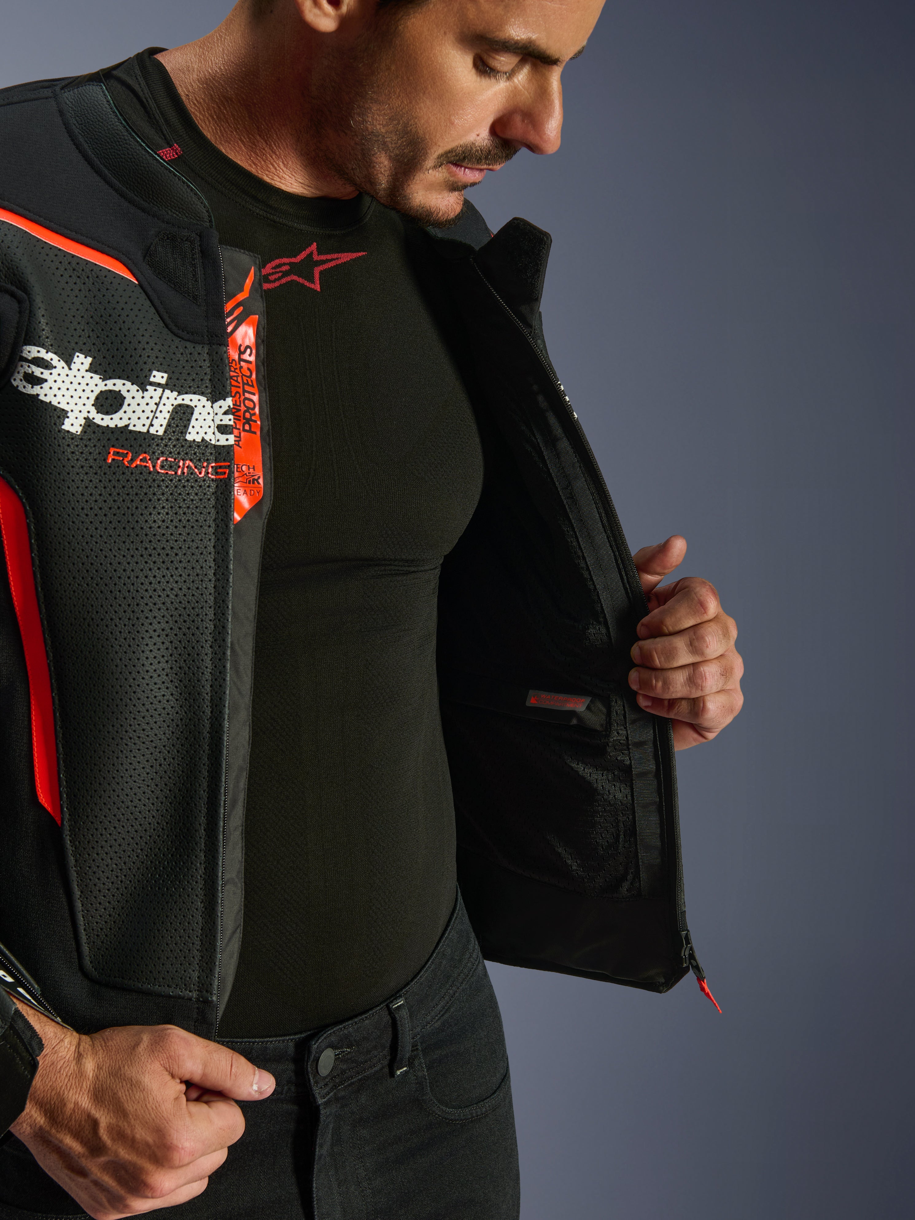 Alpinestars GP Force V2 Air Leather Jacket, Black and Red Fluo, unzipped to reveal internal waterproof pocket and branding, perforated leather multi-panel construction for airflow, worn with black Alpinestars base layer