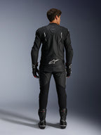 Motorcycle rider from a rear view wearing the Alpinestars Dusk Leather Jacket and Missile V3 Leather Pants, full black leather suit with white accents, jacket features 'Dusk' branding and Alpinestars logo on the back, paired with black racing boots and gloves, coordinated motorsport outfit for road racing.