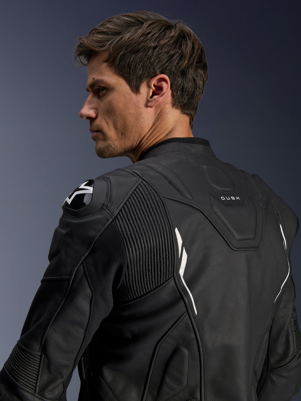 Alpinestars Dusk Leather Jacket, Black with White accents, back view on model, featuring DFS shoulder protectors with Alpinestars logo, accordion leather stretch panels for mobility, and 'DUSK' branding on the upper back, premium bovine leather motorcycle jacket for road and sport riding