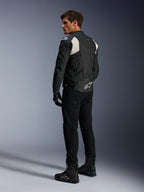 Alpinestars Dusk Airflow Leather Jacket, Black and White, rear view of model wearing the perforated leather jacket with matching black pants and boots, featuring white accordion stretch panels and bold logo on the lower back, sport motorcycle riding gear