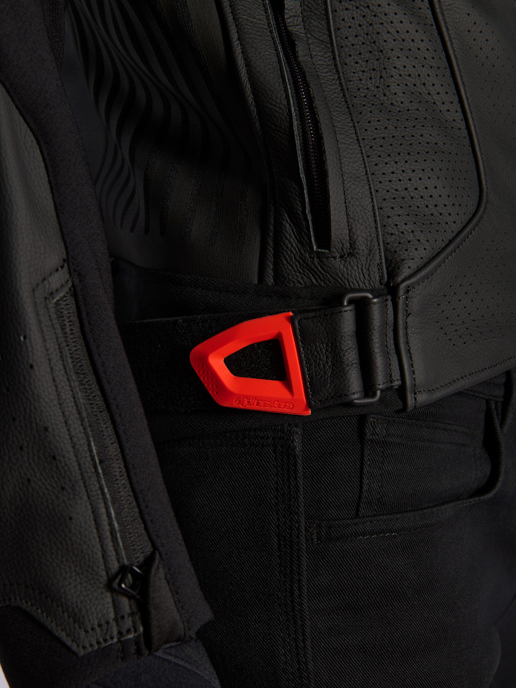 Alpinestars GP Plus R V4 Airflow Leather Jacket close-up, black perforated leather with a vibrant red fluo hook-and-loop waist adjustment strap, featuring a zippered side pocket and ergonomic textured panels.