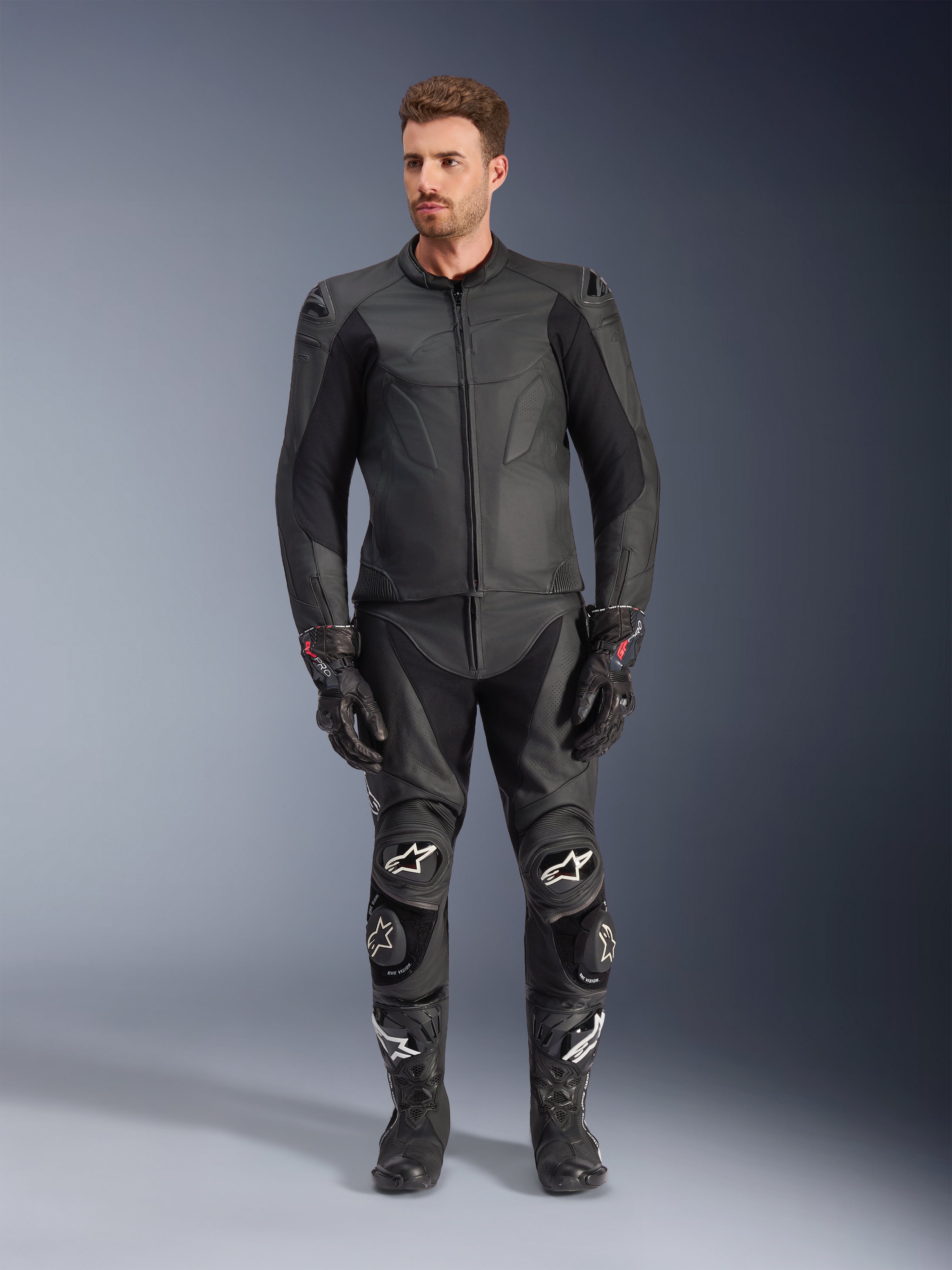 Alpinestars Caliber Leather Jacket, Black motorcycle jacket, worn with matching racing pants, gloves and boots, featuring a sleek design with tonal logos, stretch panels on the sleeves, and protective shoulder sliders, professional studio setting